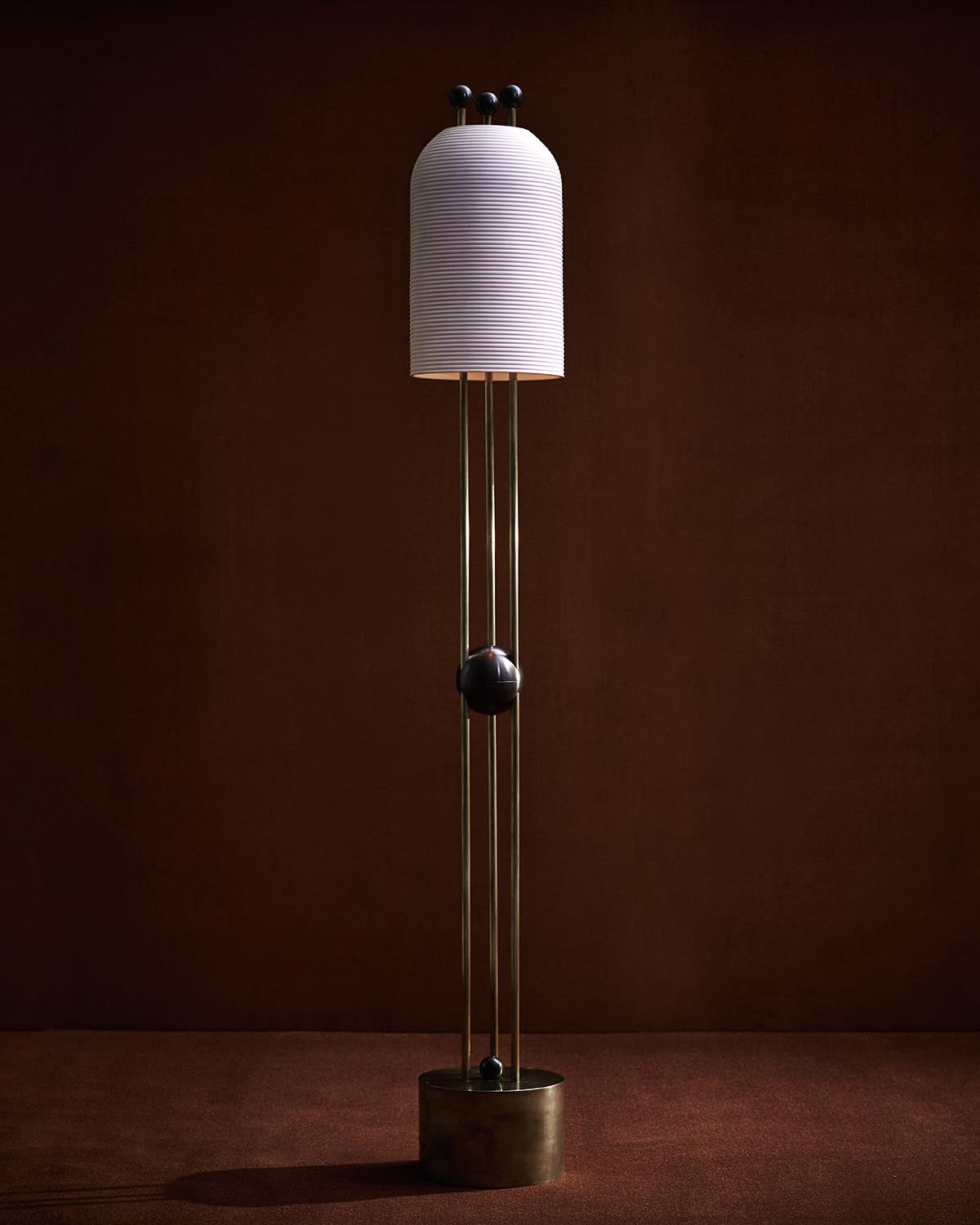 Tall floor lamp with a ribbed cylindrical white shade supported by three slim brass rods and a round base