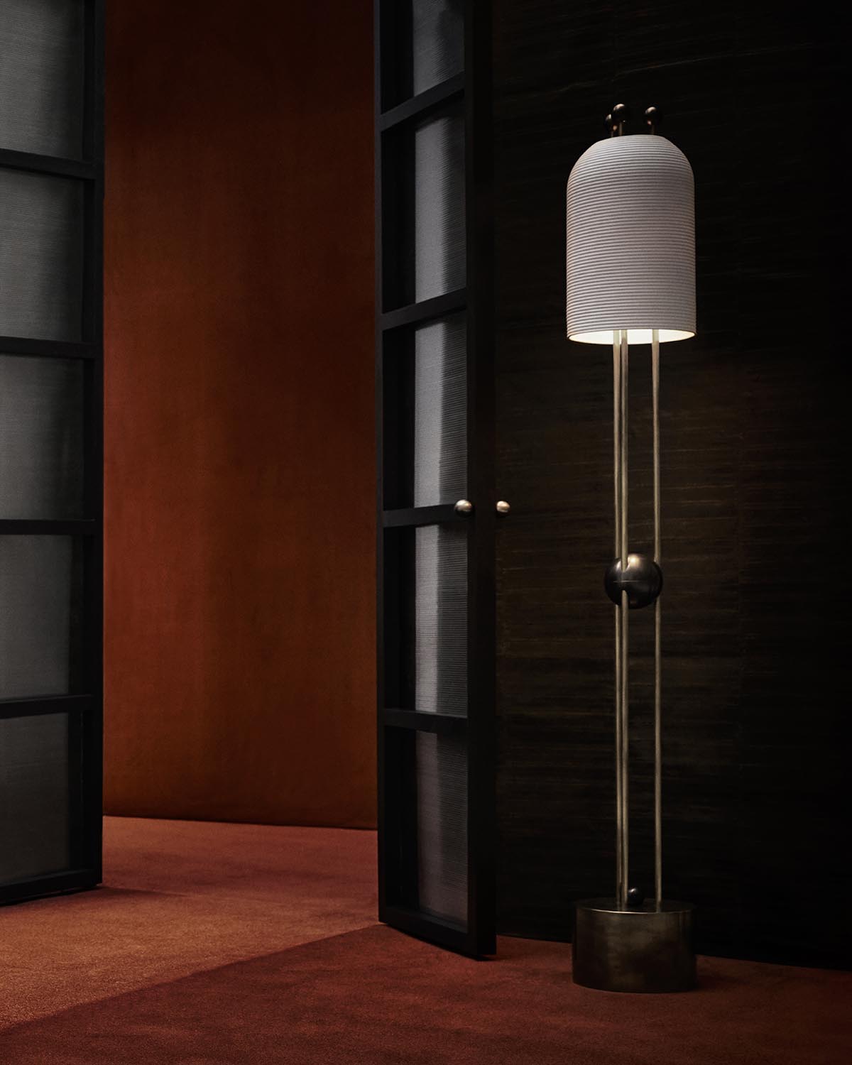 Tall floor lamp with ribbed white cylindrical shade and slender metal frame in dark interior setting