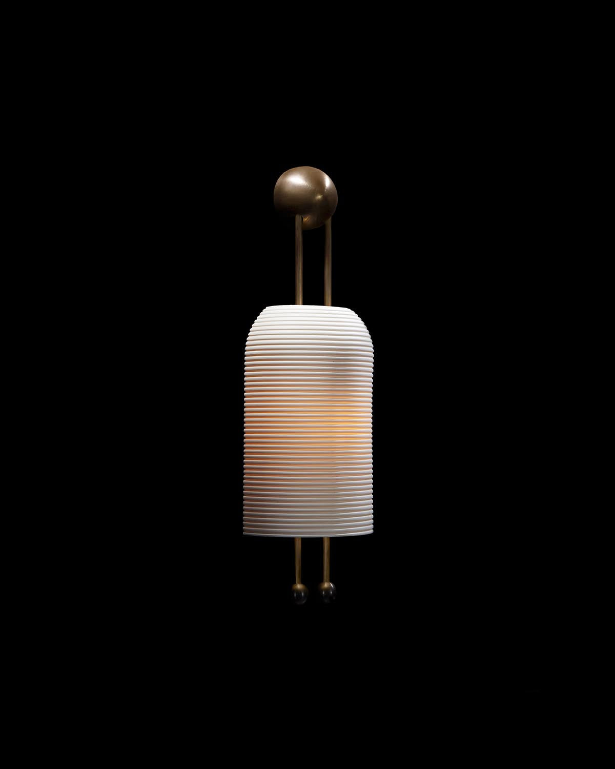 Wall-mounted sconce with ribbed white cylindrical shade and aged brass suspension against black background
