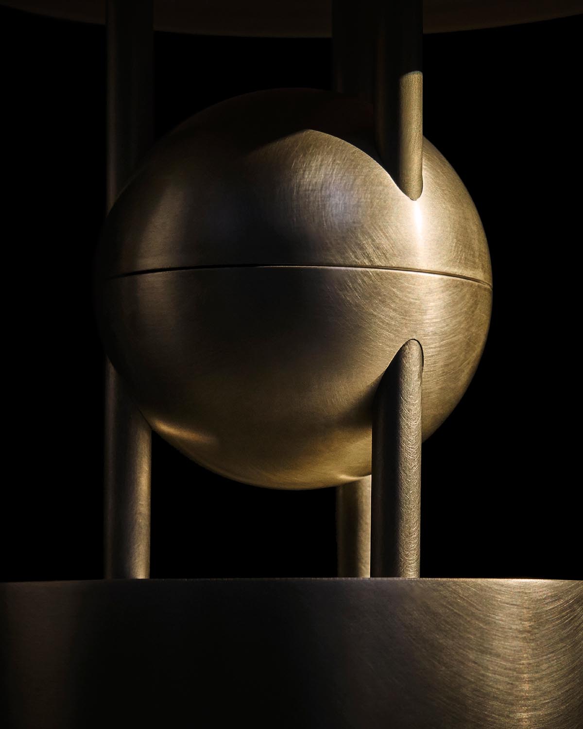 Close-up of a brushed metal spherical element supported by three vertical rods against a black background