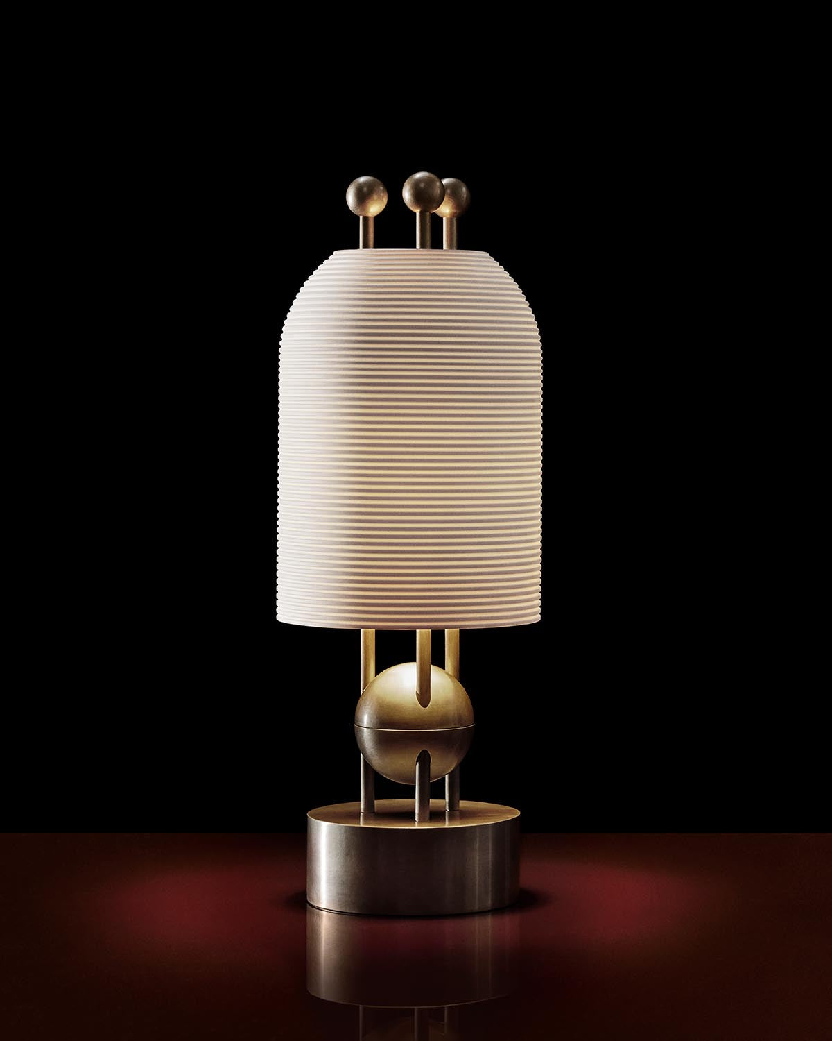 Modern table lamp with ribbed cylindrical shade and brass spherical accents on a reflective surface against black background