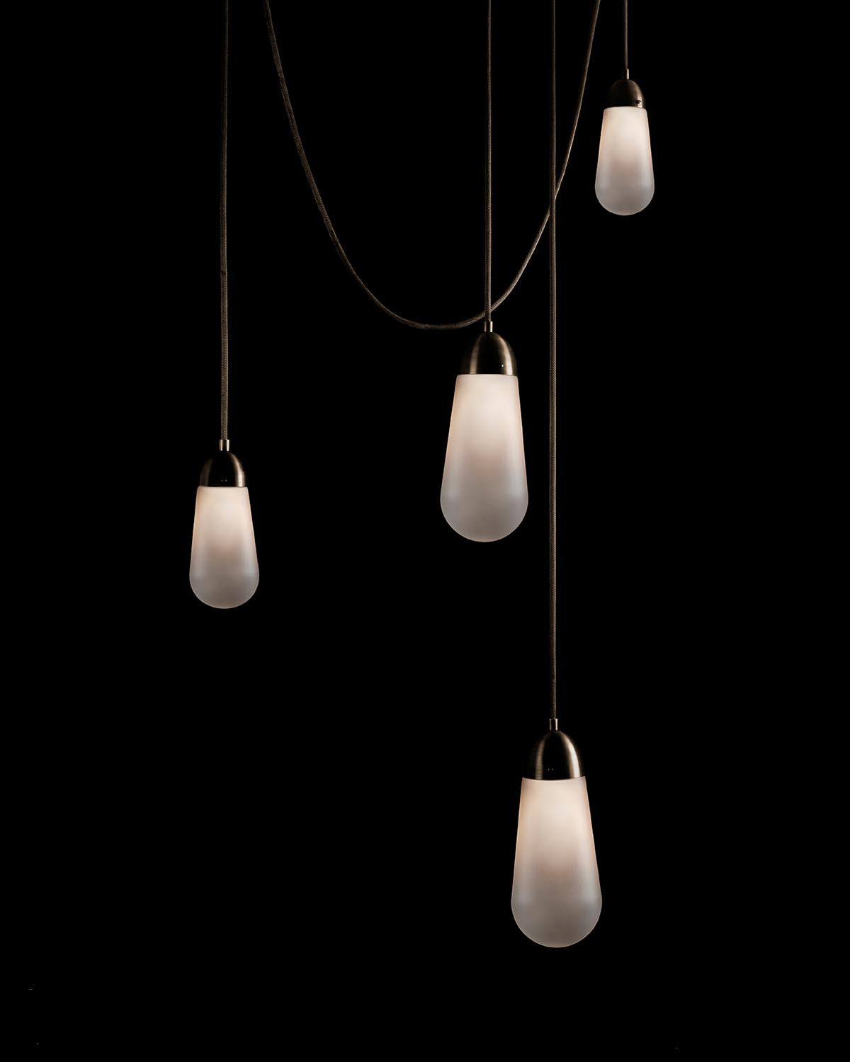 Four elongated frosted glass pendant lights hanging at varying heights against a black background