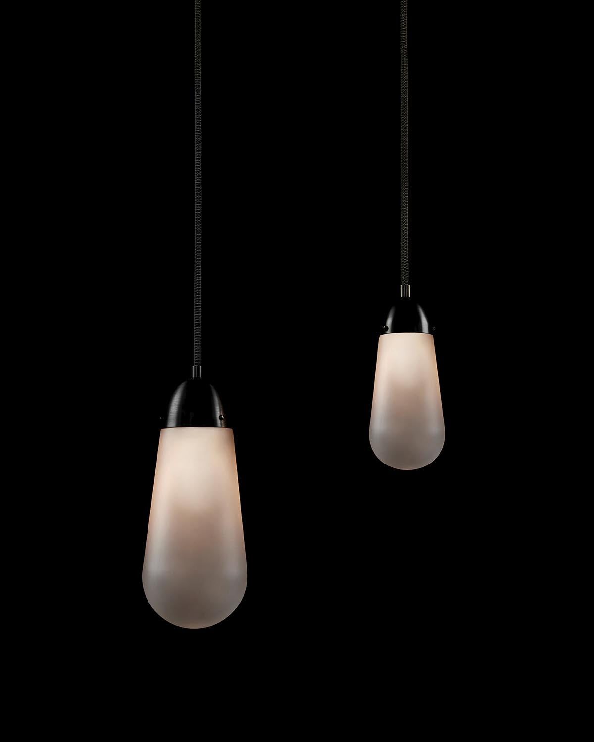 Two elongated frosted glass pendant lights with black metal caps suspended against a black background