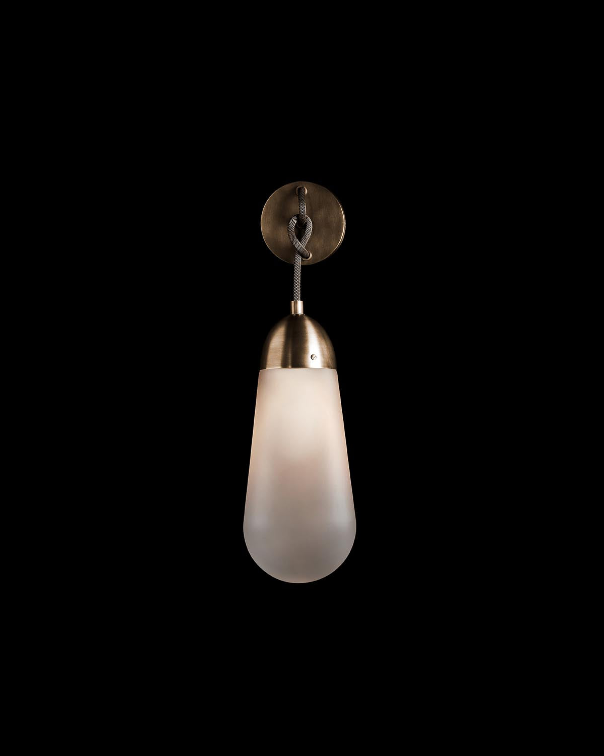 Single pendant wall sconce with frosted elongated glass shade and antique brass finish mount on black background