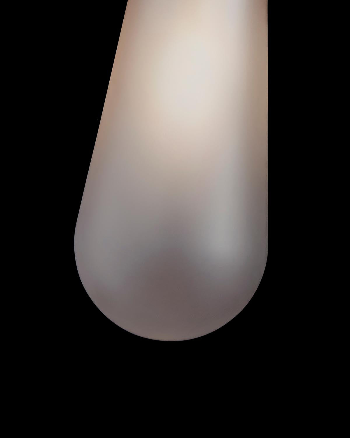 Close-up of elongated frosted glass sconce with soft warm light glowing against a black background