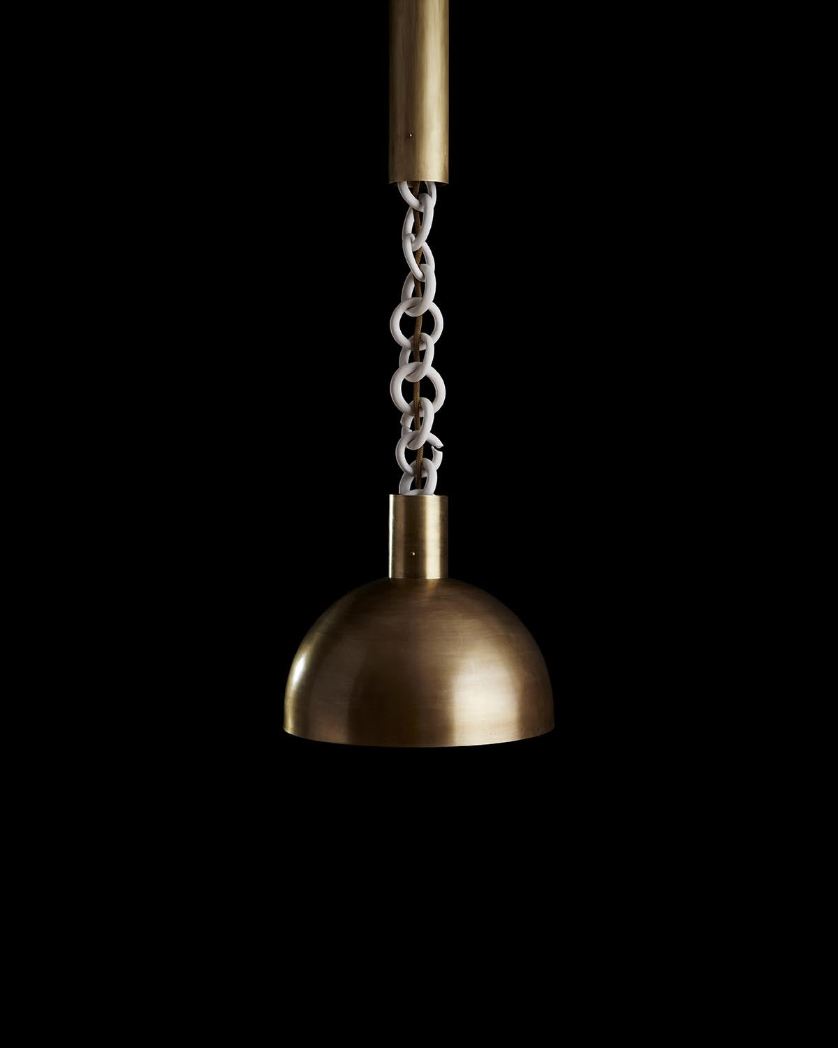 Close-up of a brass dome pendant light suspended by white linked chain against a black background