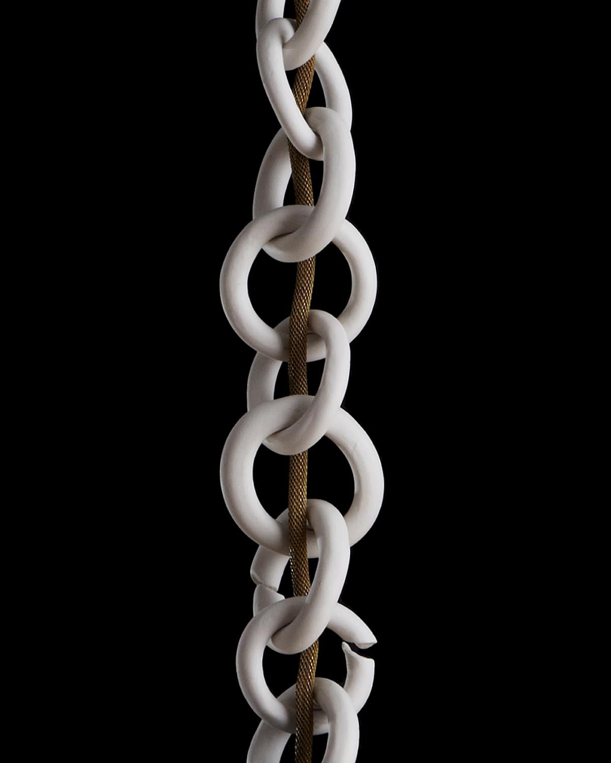 Close-up of large white ceramic chain links intertwined with a textured brown rope against a black background