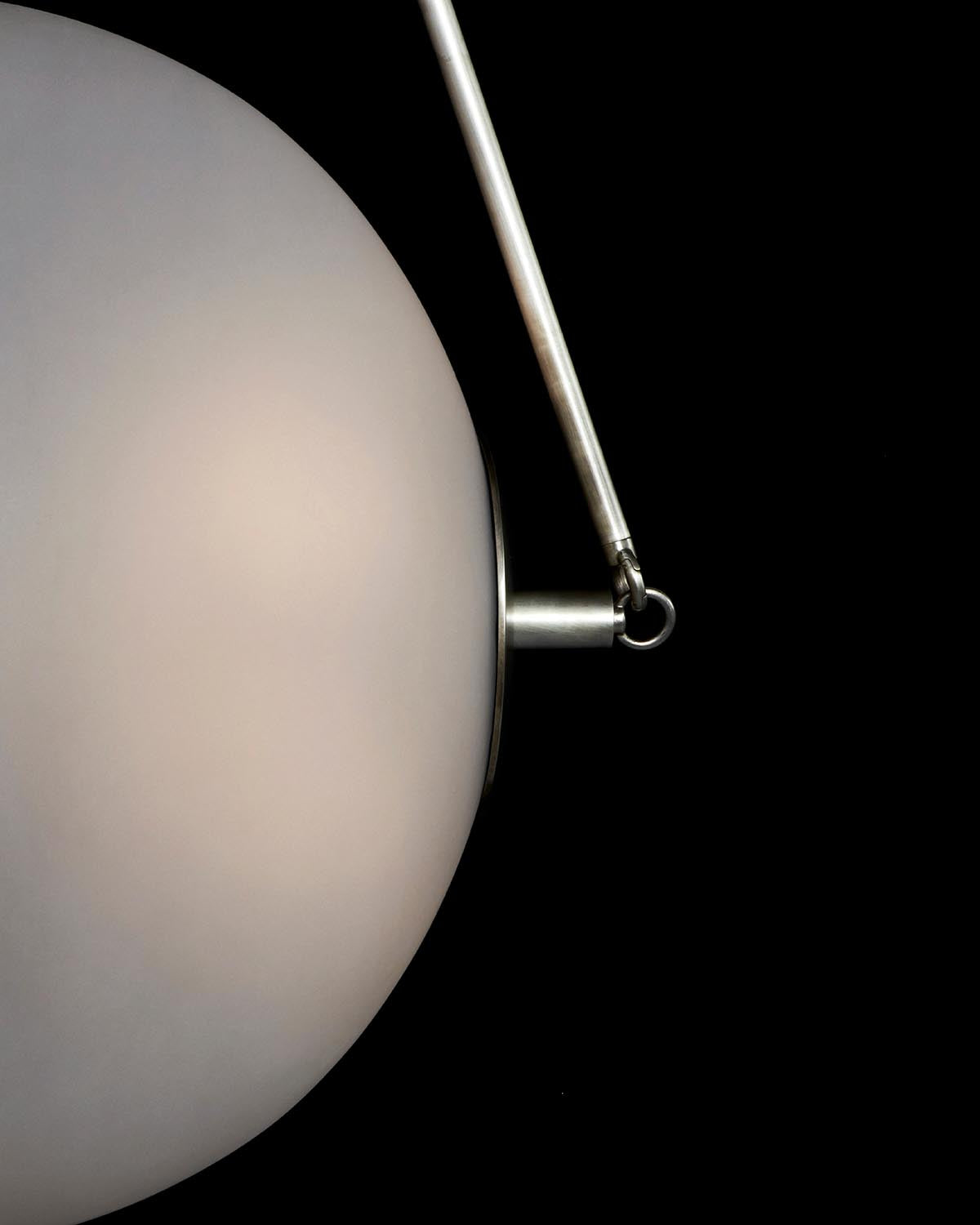 Close-up of a round white frosted glass lamp shade with a silver metal arm against a black background