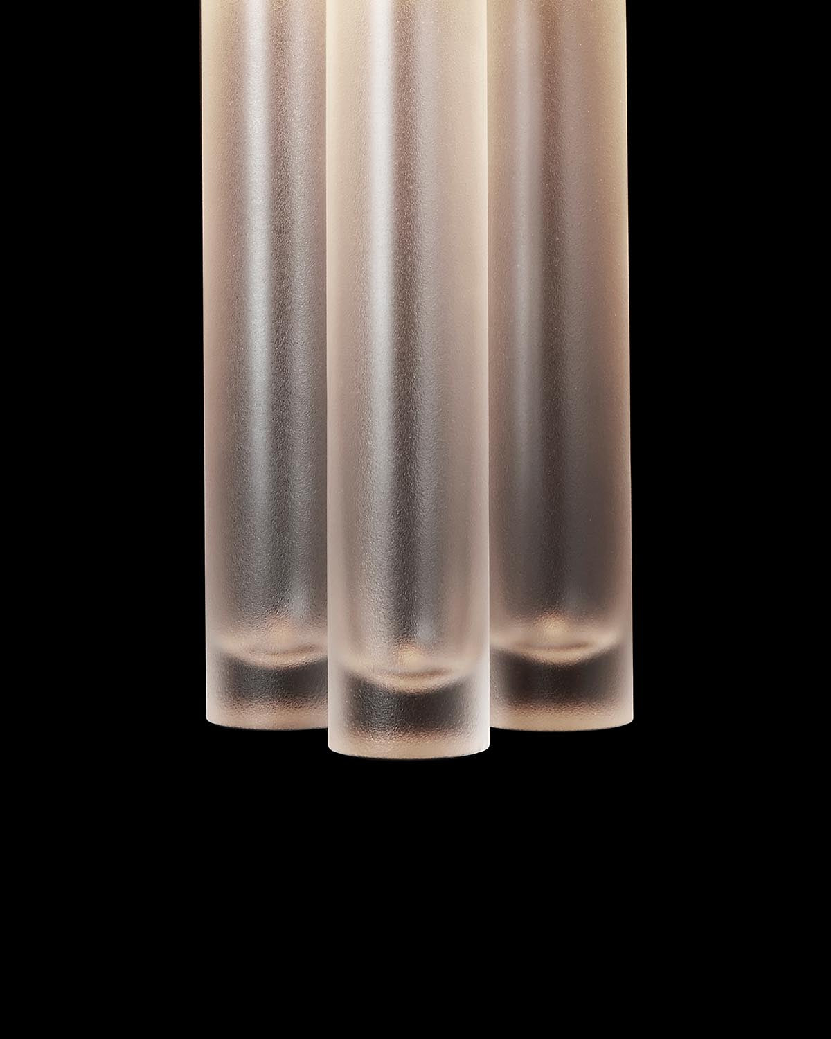 Close-up of three frosted glass cylinders with soft lighting against a black background