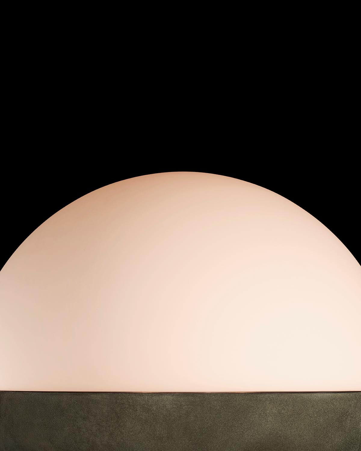 Softly lit half-sphere lamp with smooth beige surface set on a dark textured base against black background