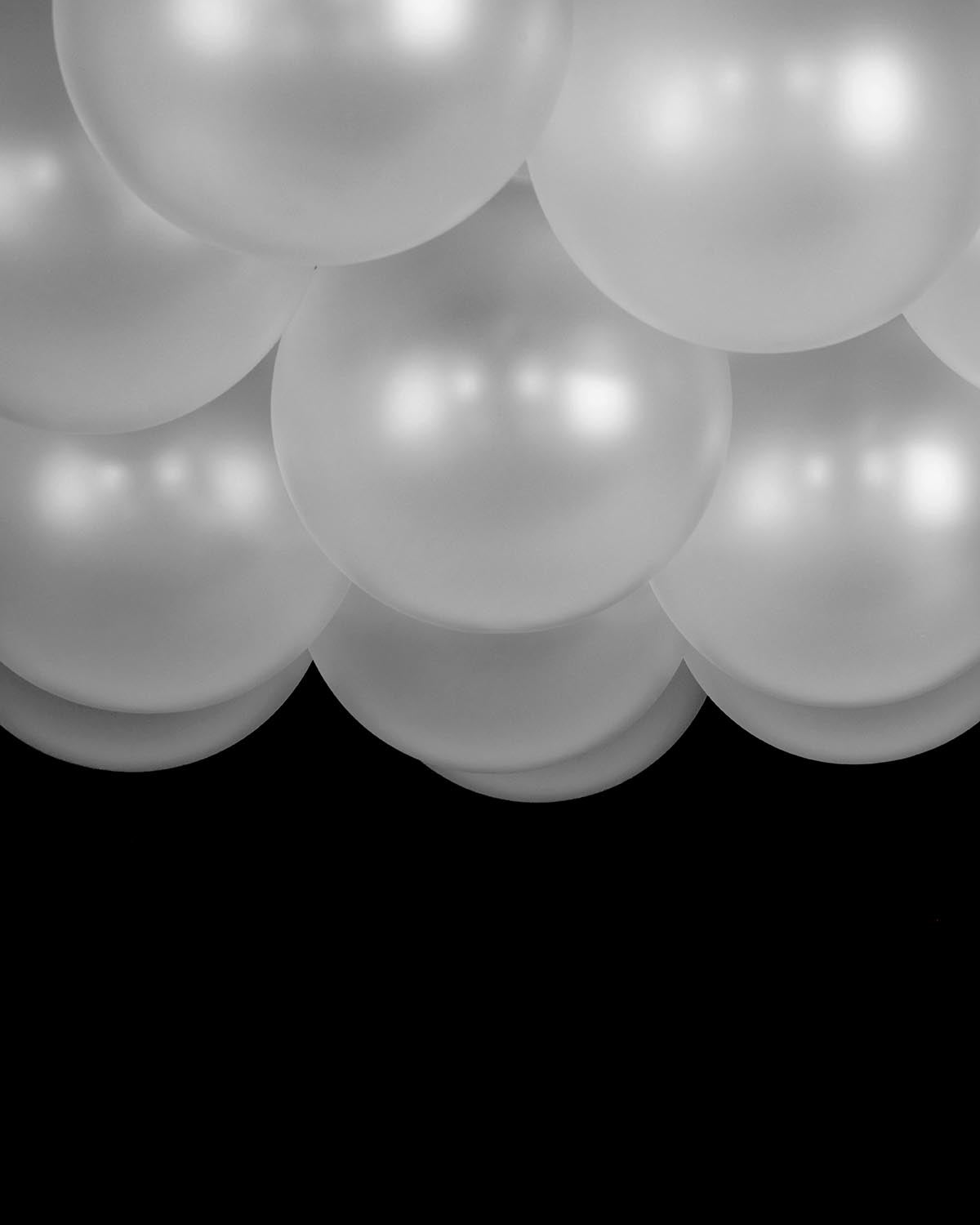 Close-up view of clustered semi-transparent white balloons with soft lighting against a black background