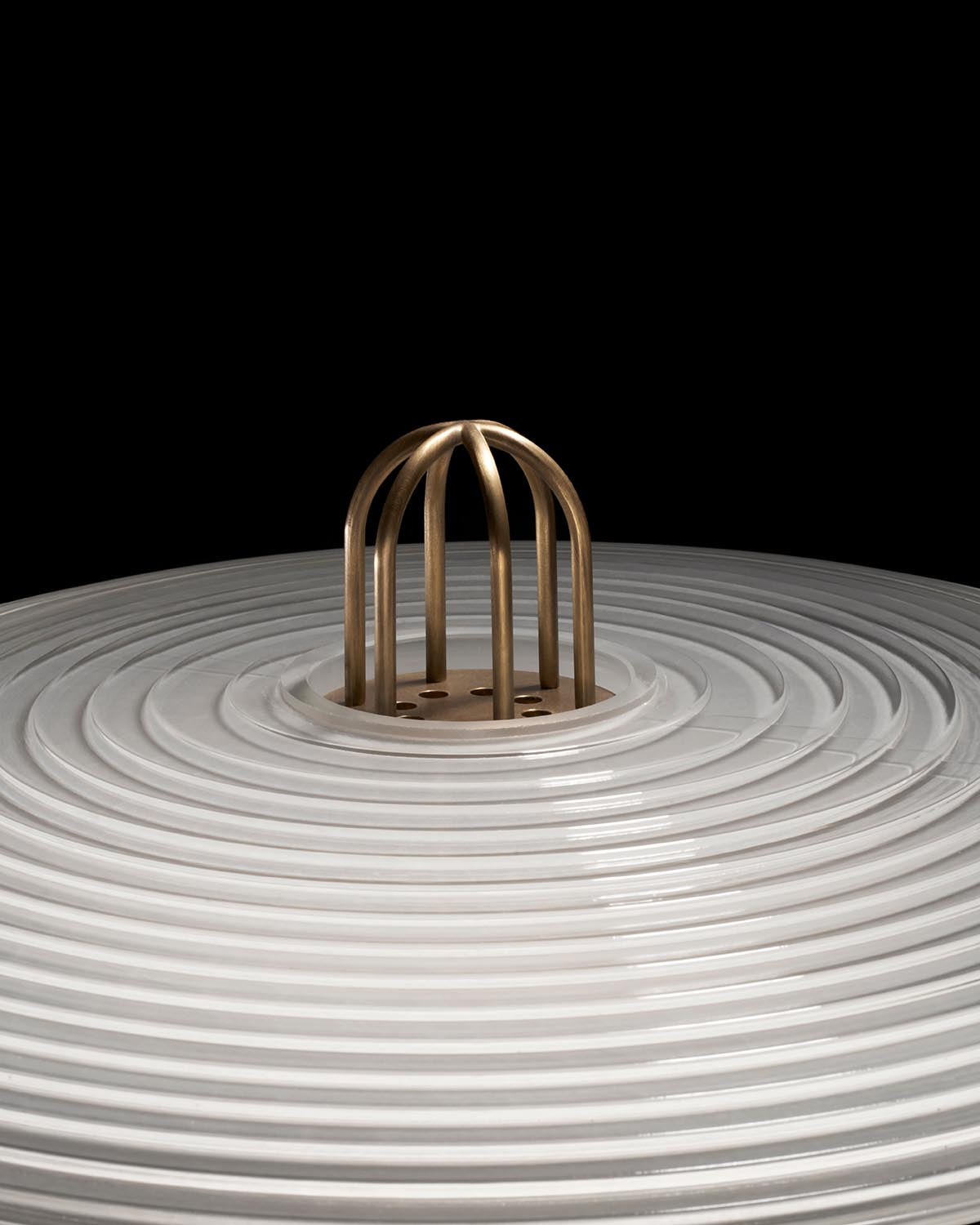 Close-up of a white concentric ring surface with a central brass cage-like structure against a black background