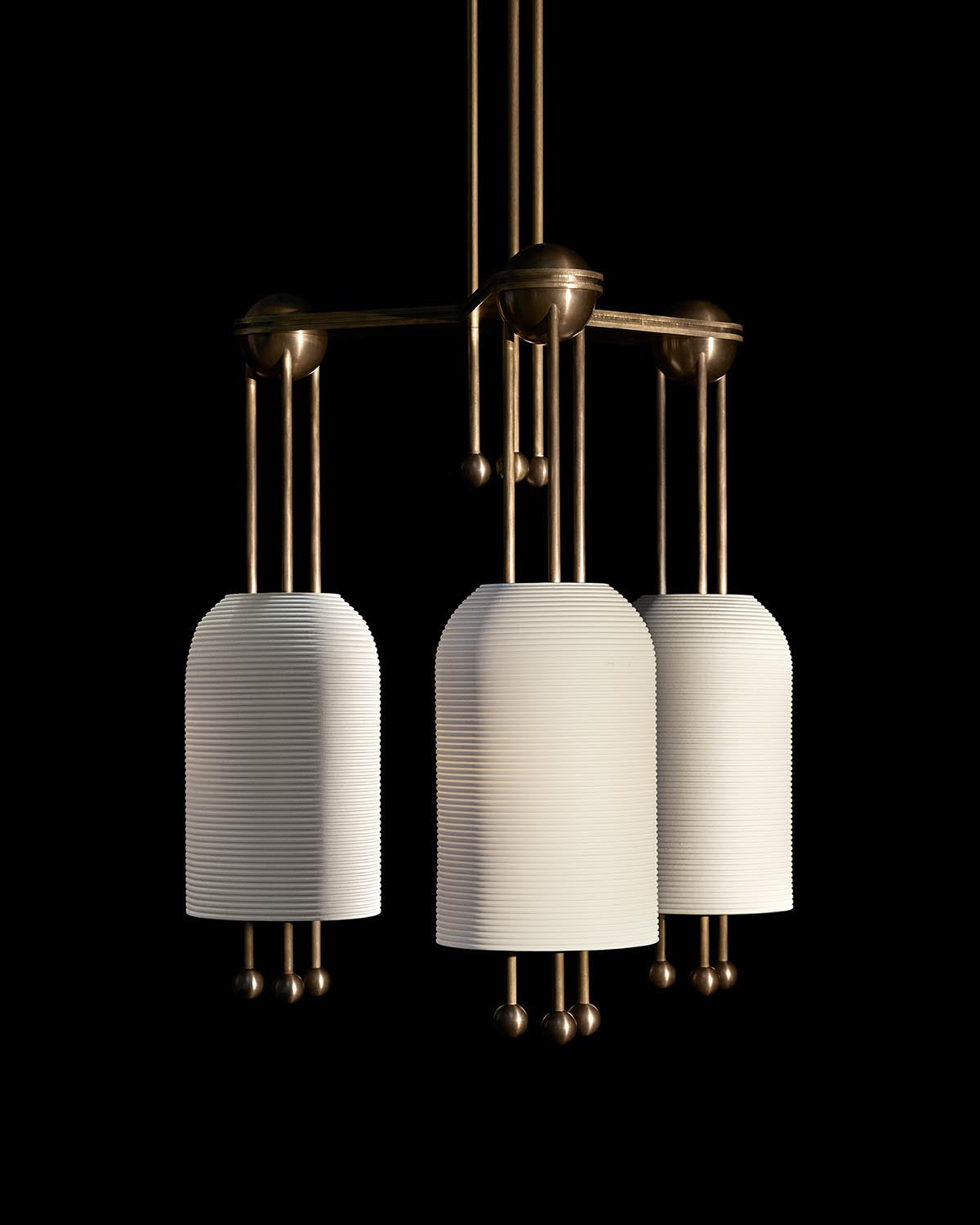 Three cylindrical pendant lights with ribbed white shades and brass fixtures suspended against a black background