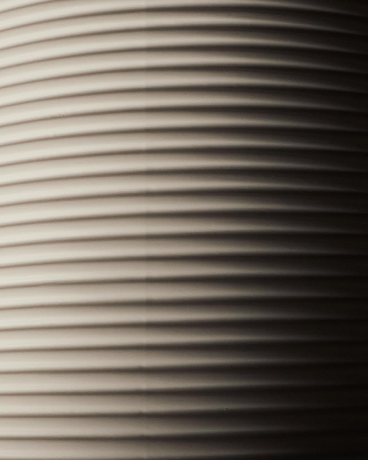Close-up of a curved surface with evenly spaced horizontal ridges, illuminated to show light and shadow contrast