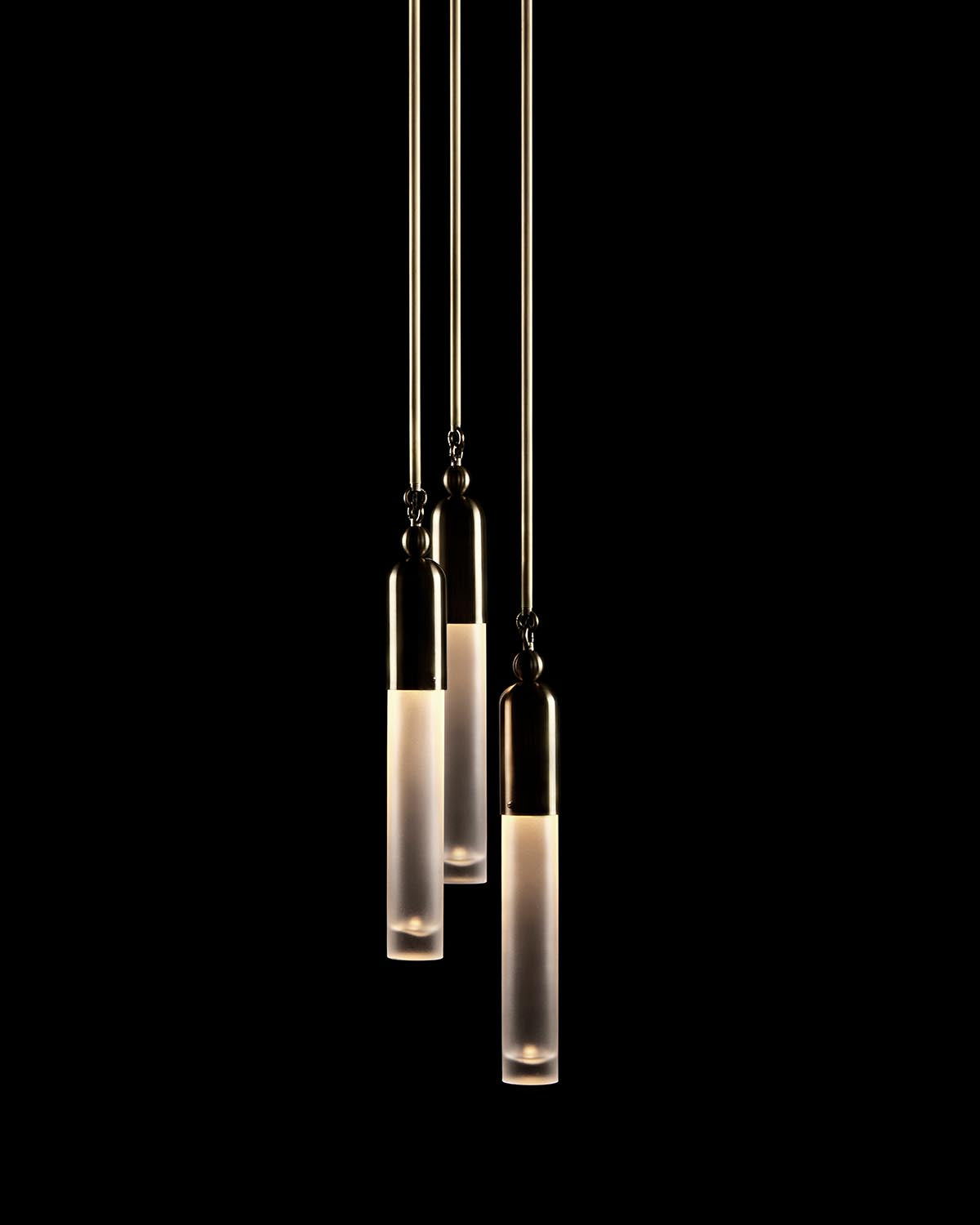 Three elongated pendant lights with frosted glass and brass fittings hanging against a black background