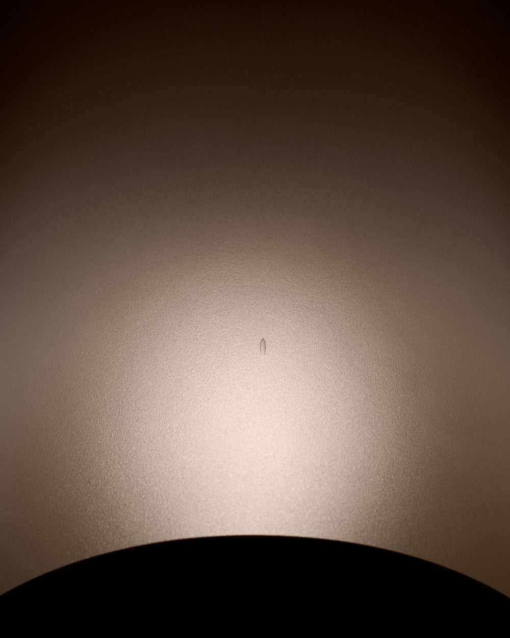 Close-up of a curved matte surface with a small central scratch illuminated softly from below against a dark background