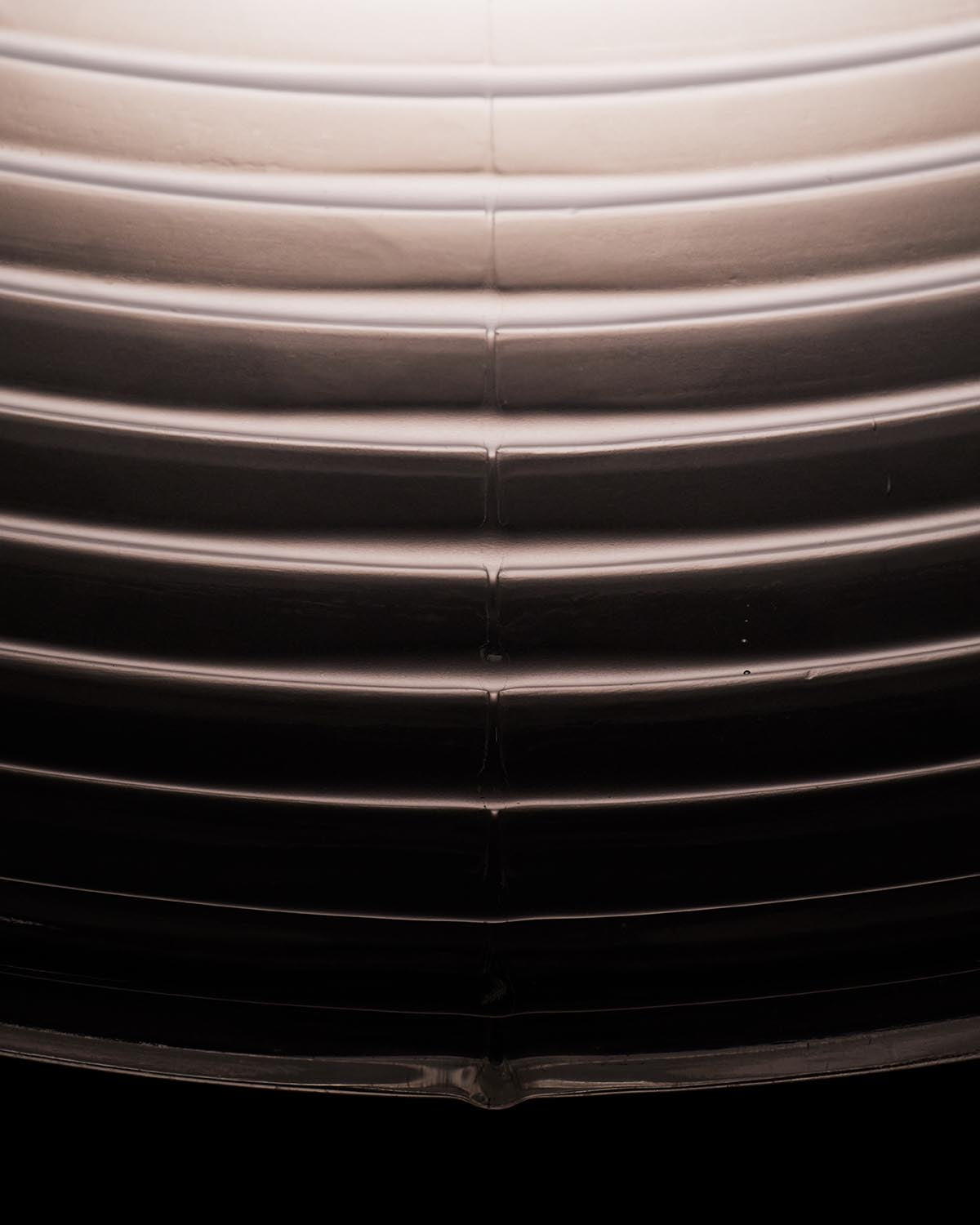 Close-up of curved, smooth metallic surface with horizontal ridges and a central vertical seam against a dark background