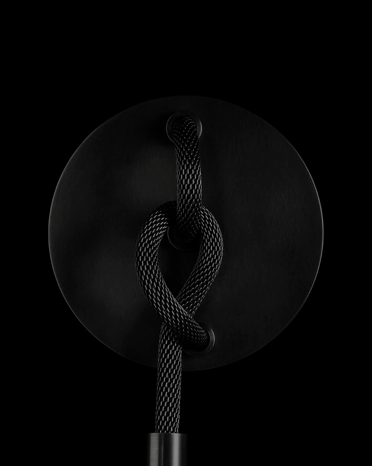Black woven rope tied in a knot around a matte black circular base against a dark background