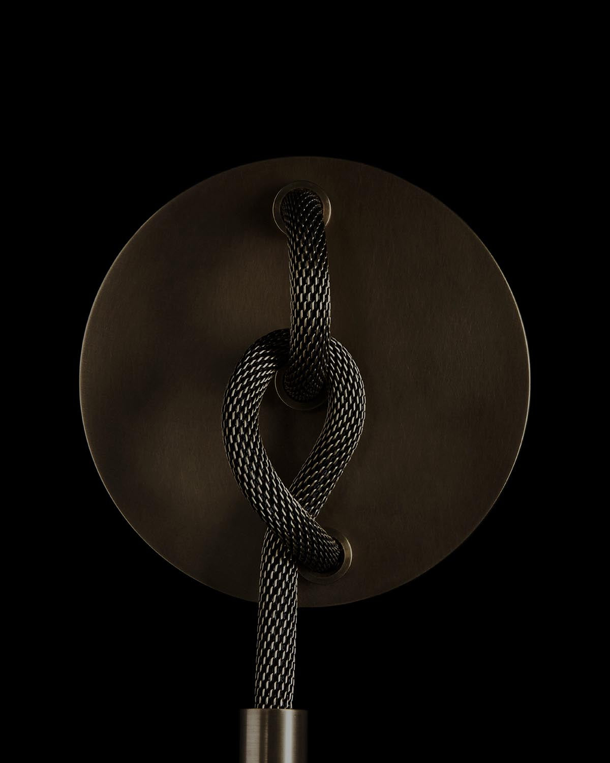 Close-up of a dark metal circular base with a black and white braided cord looped through two holes against a black background