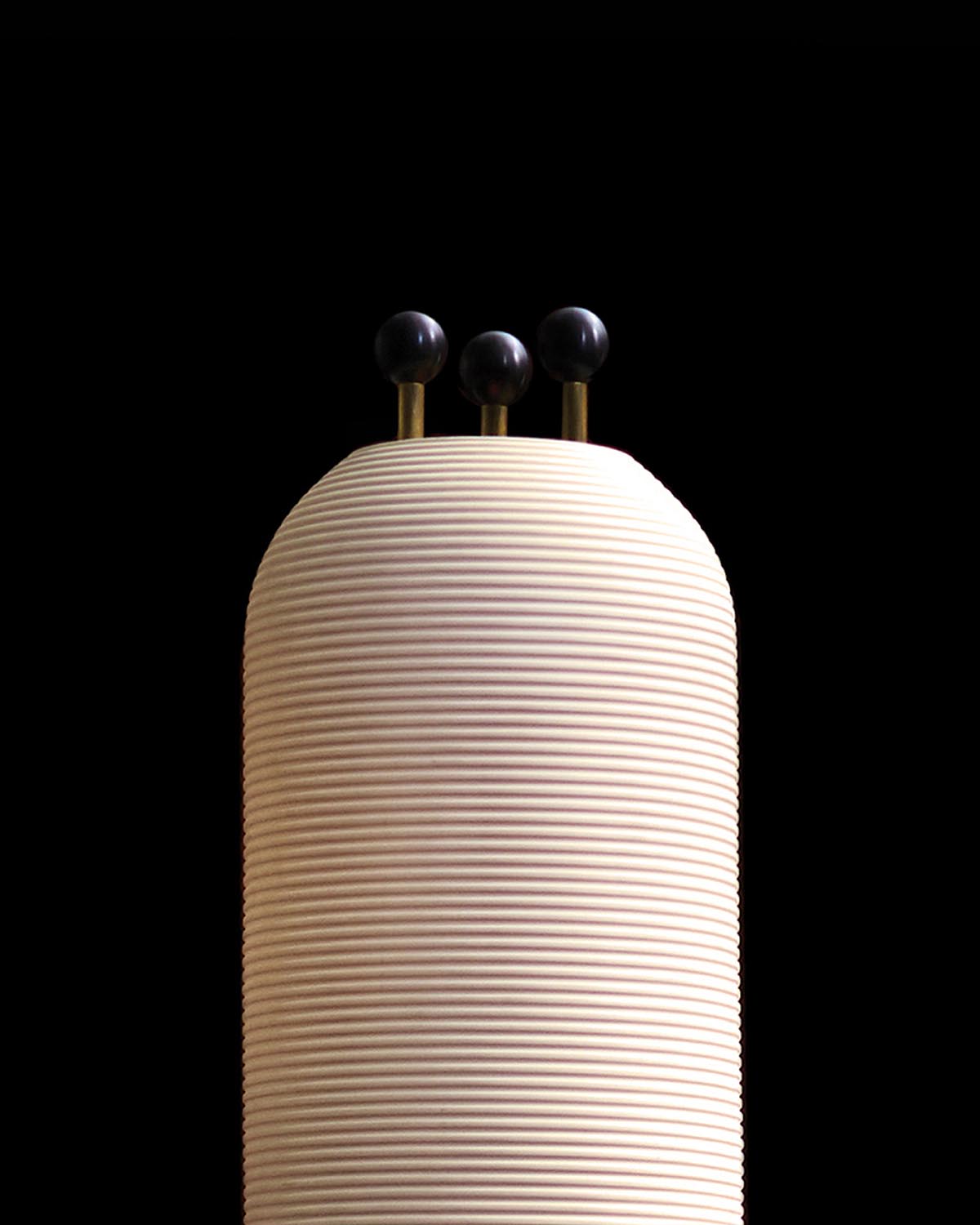 Close-up of a white ribbed cylindrical object with three black spheres mounted on thin brass rods against a black background