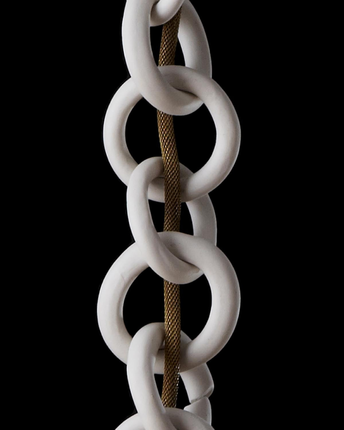 Close-up view of large white ceramic chain links intertwined with a textured brown rope against a black background