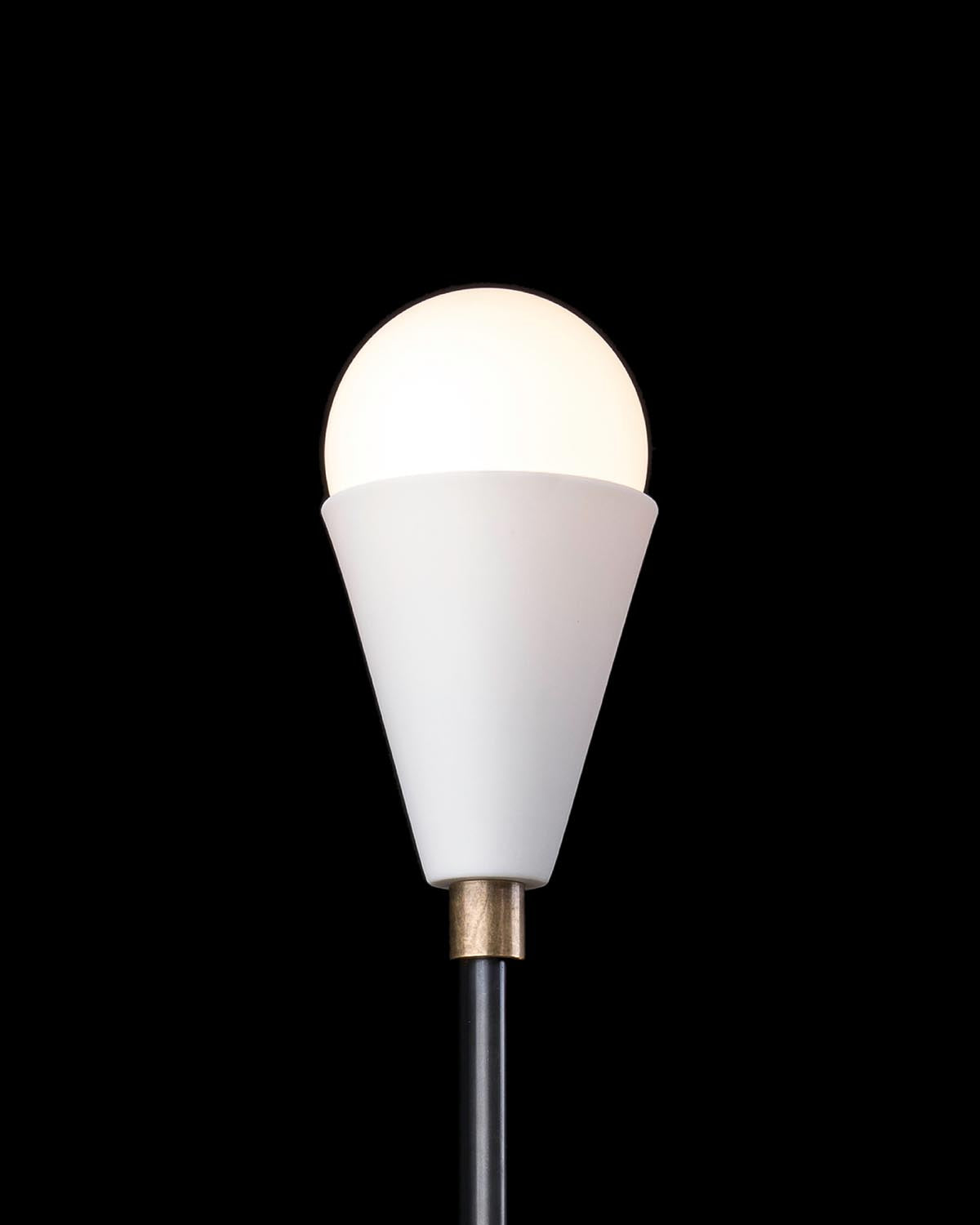Close-up of a modern floor lamp with a glowing white spherical bulb in a white conical shade on a black background