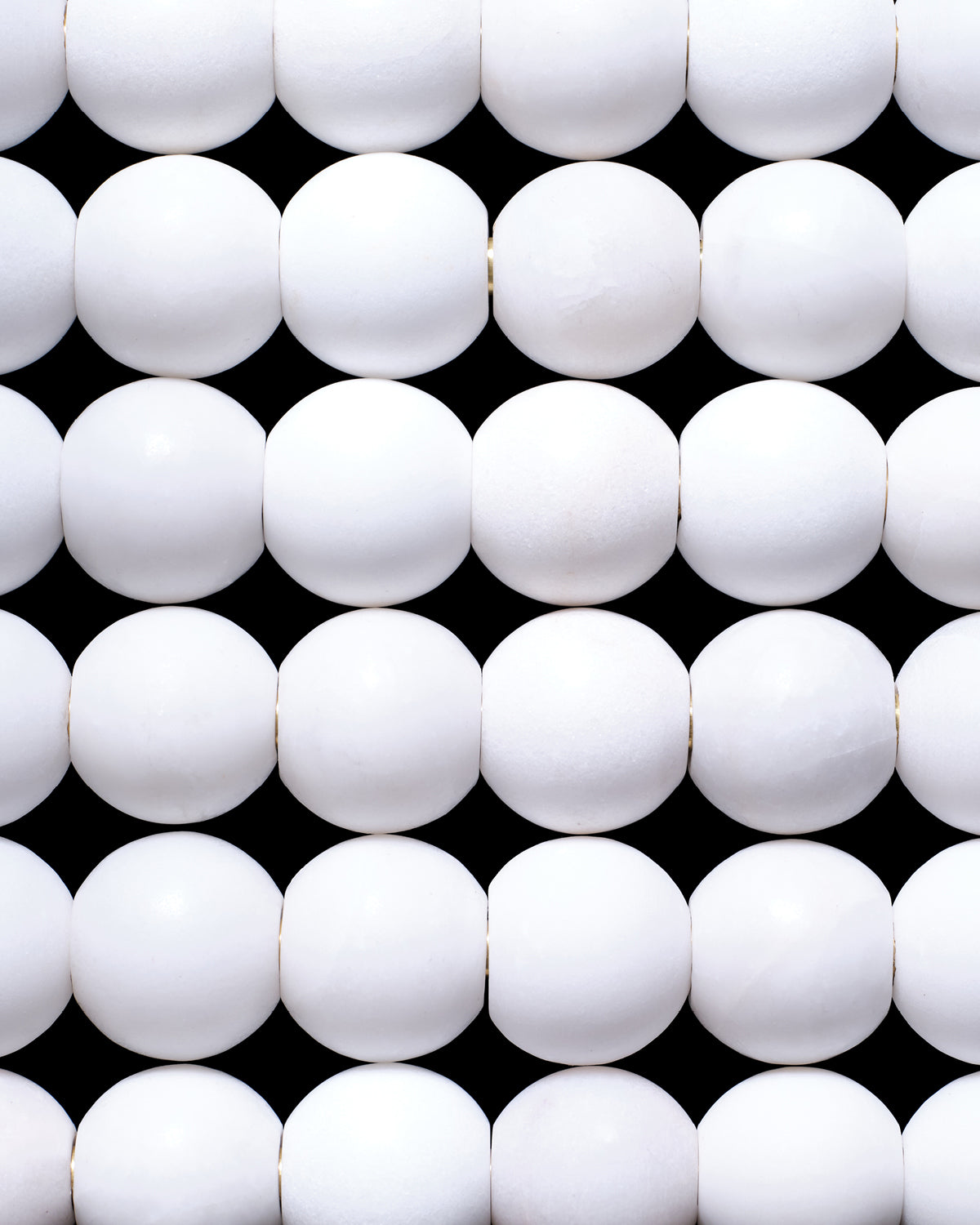Close-up of evenly spaced smooth white spherical beads arranged in horizontal rows on a black background