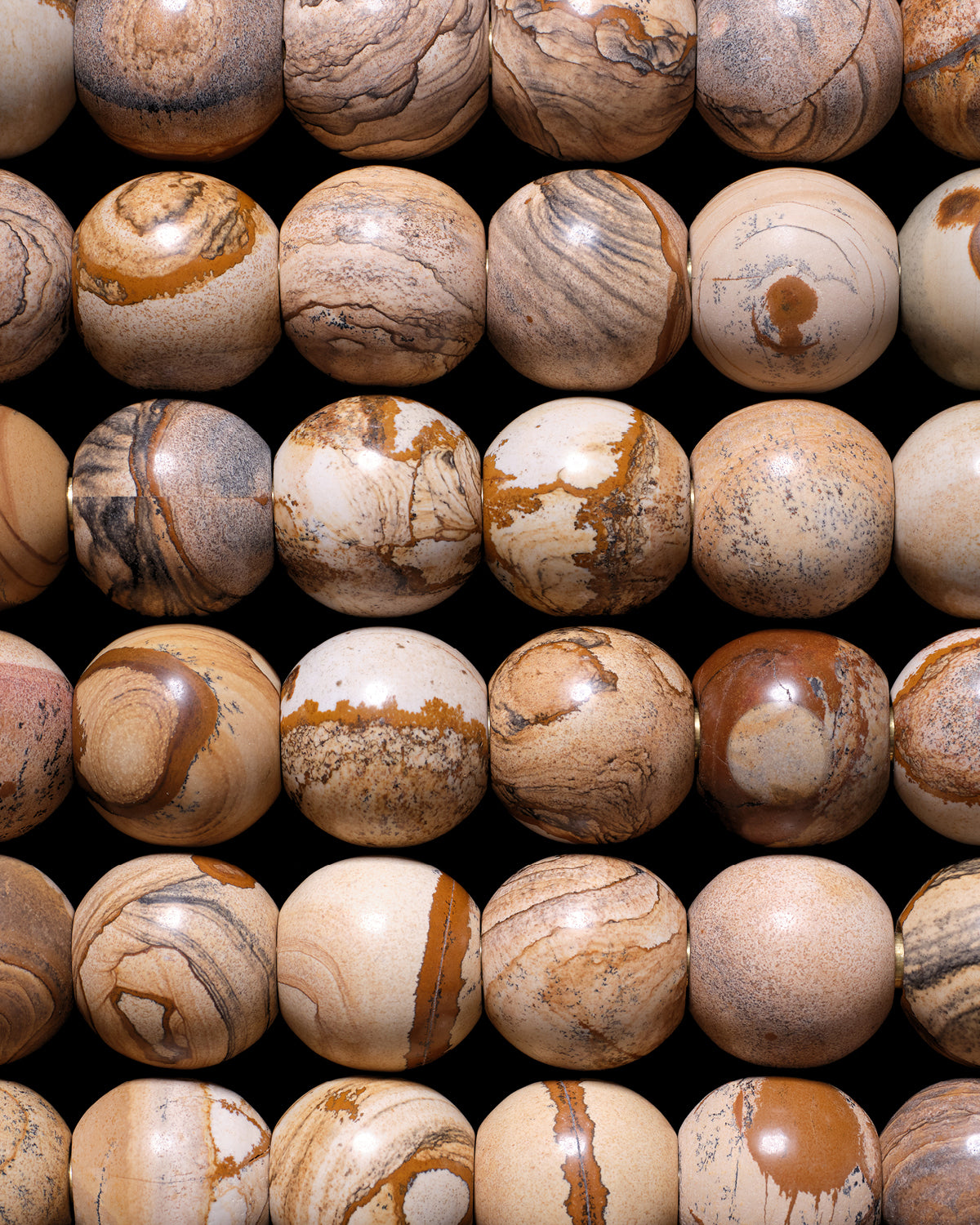 Close-up of multiple polished round stone spheres with natural beige, brown, and tan patterns arranged in rows on a black background