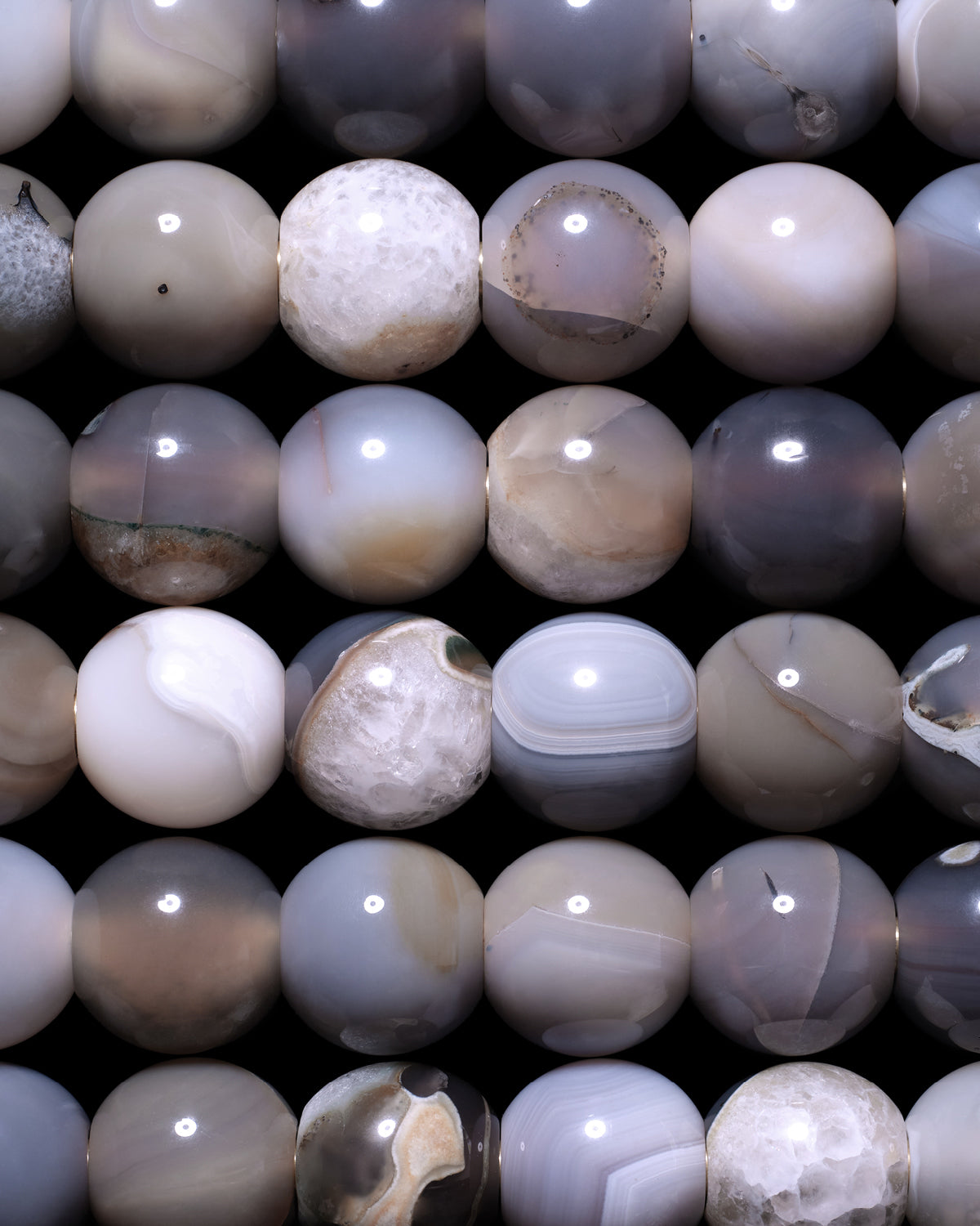 Close-up of polished round stones in muted gray and beige tones arranged in a grid pattern on a dark background