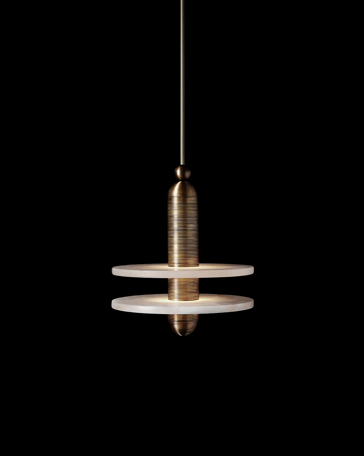 Brushed brass cylindrical pendant light with two flat disc shades suspended against black background