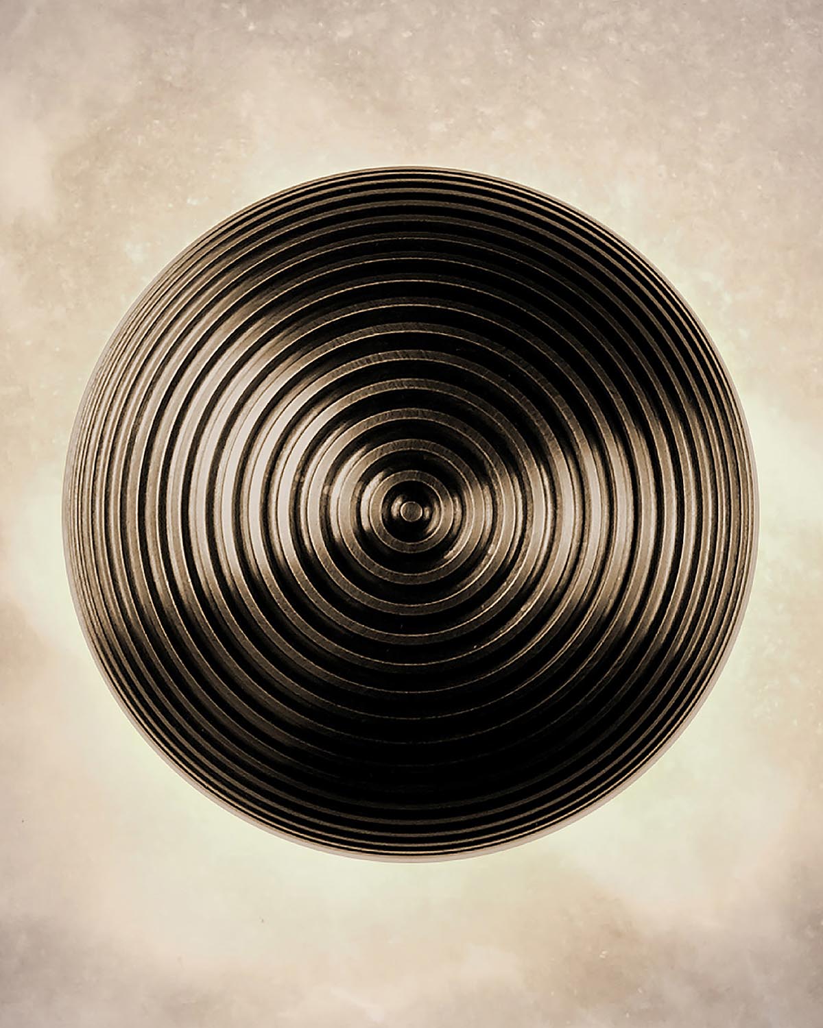 Top-down view of a circular pendant light with concentric ridges and a dark bronze finish against a neutral background