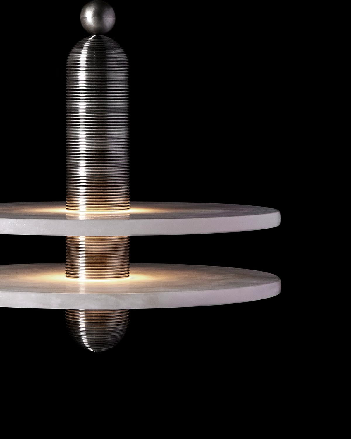Close-up of a modern pendant light with stacked circular stone discs and illuminated cylindrical metal fixture against black background