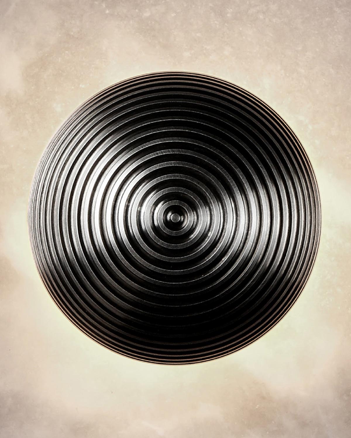 Top-down close-up of a black circular pendant light with concentric ridges illuminated against a beige textured background