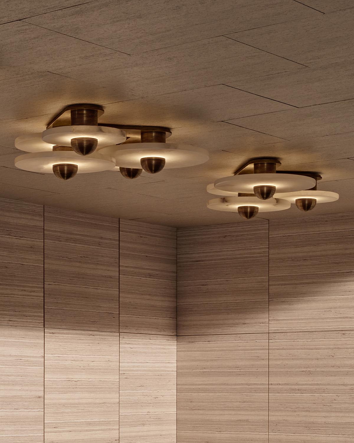 Close-up of two ceiling light fixtures with layered circular glass and bronze accents in a wood-paneled room