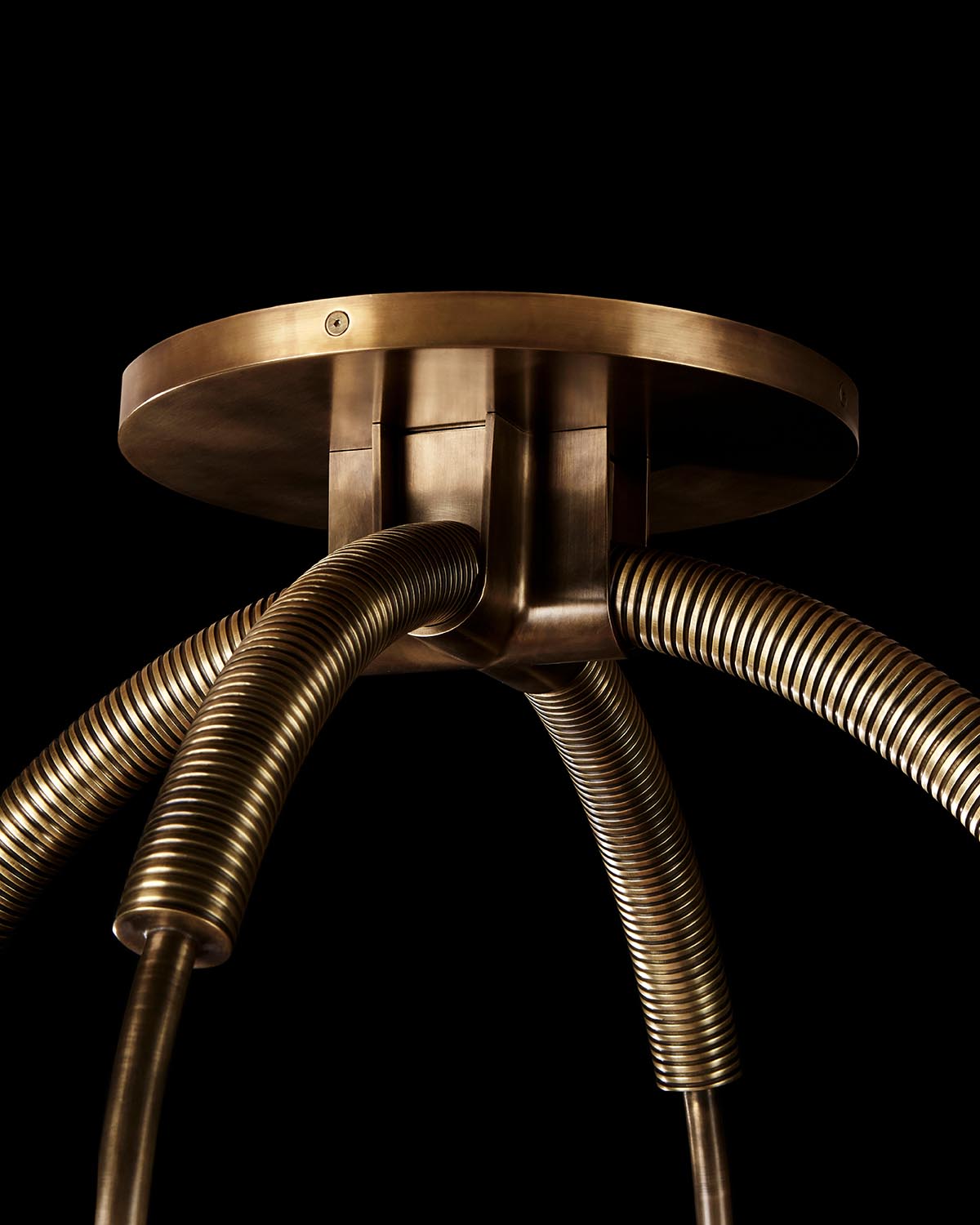 Close-up of a brass ceiling mount with four flexible corrugated metal pendant arms on a black background