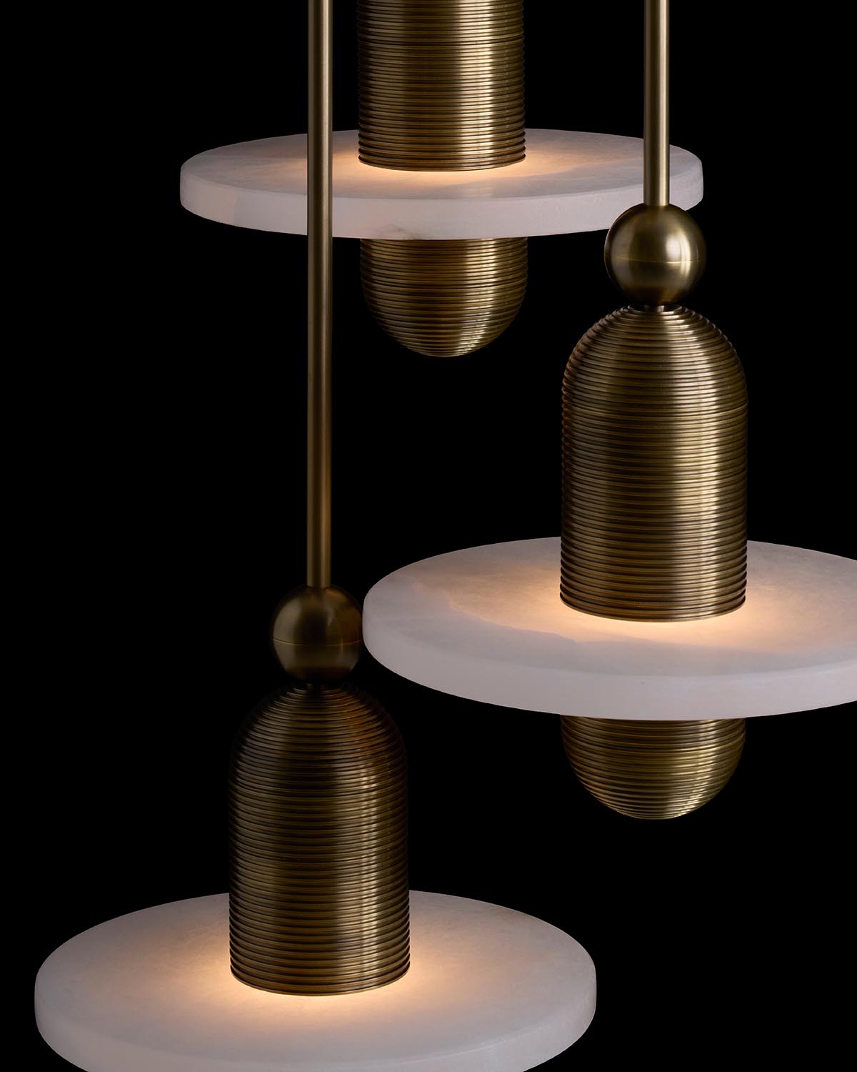 Close-up of modern pendant lights with ribbed brass shades and white circular diffusers against black background