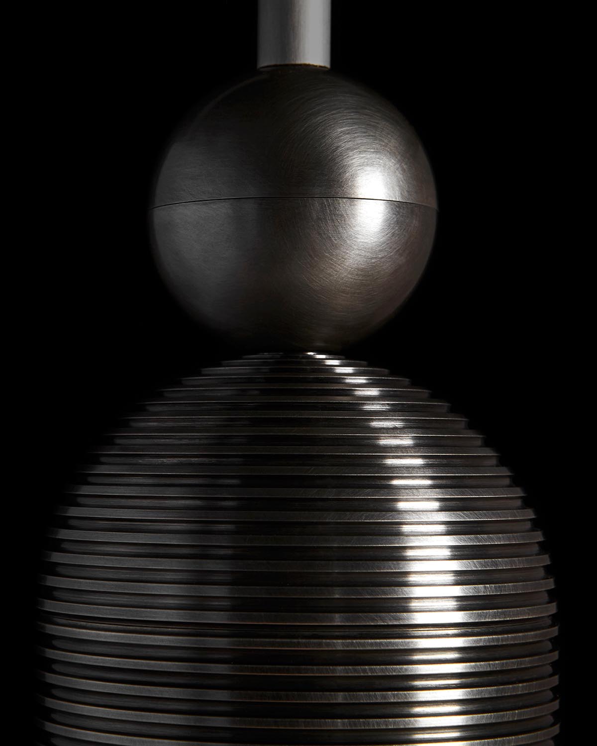 Close-up of a metallic sculpture featuring a smooth sphere atop a ribbed conical base against a dark background