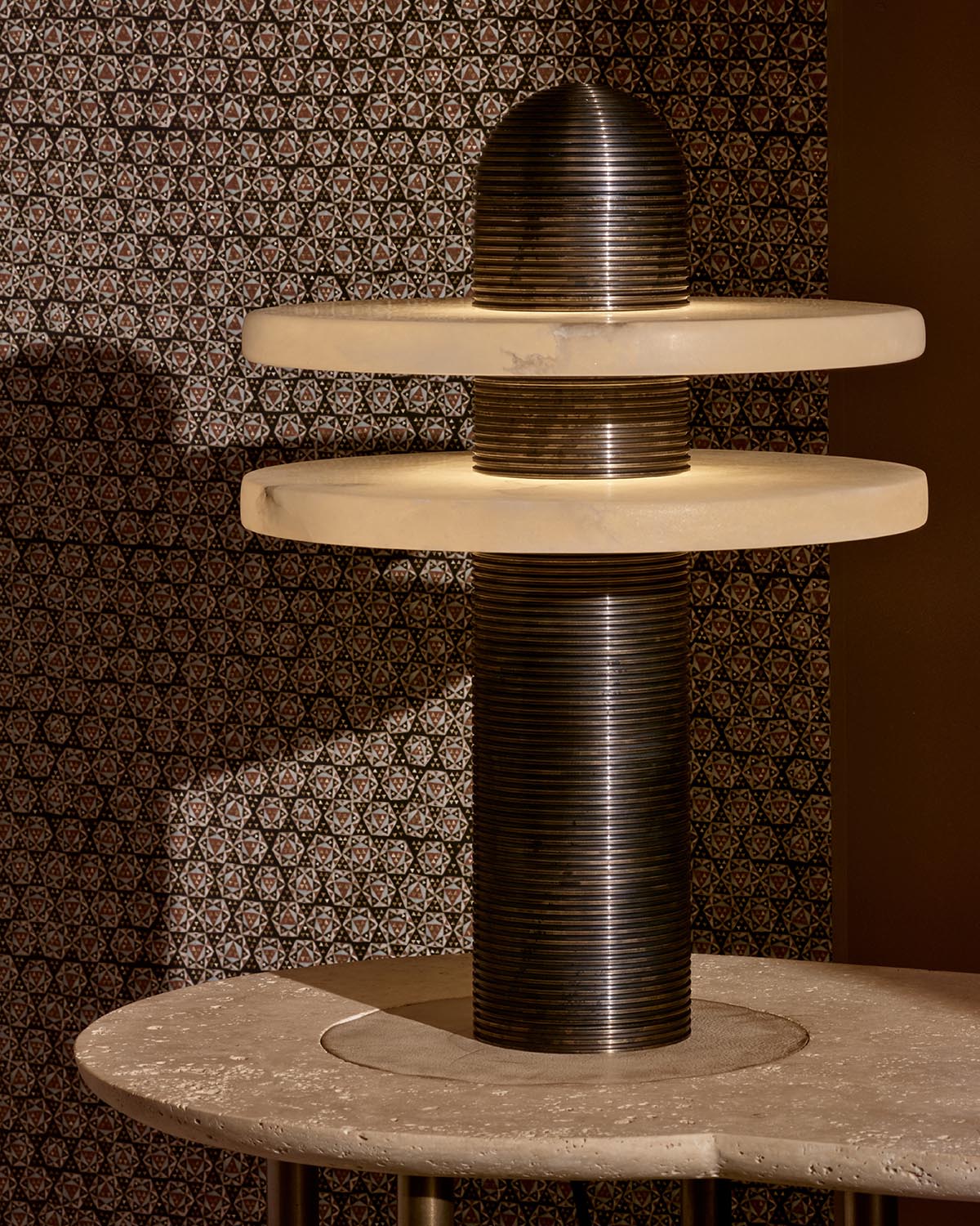 Close-up of MEDIAN table lamp with dark ribbed cylindrical base and two thick circular stone shades against patterned wall