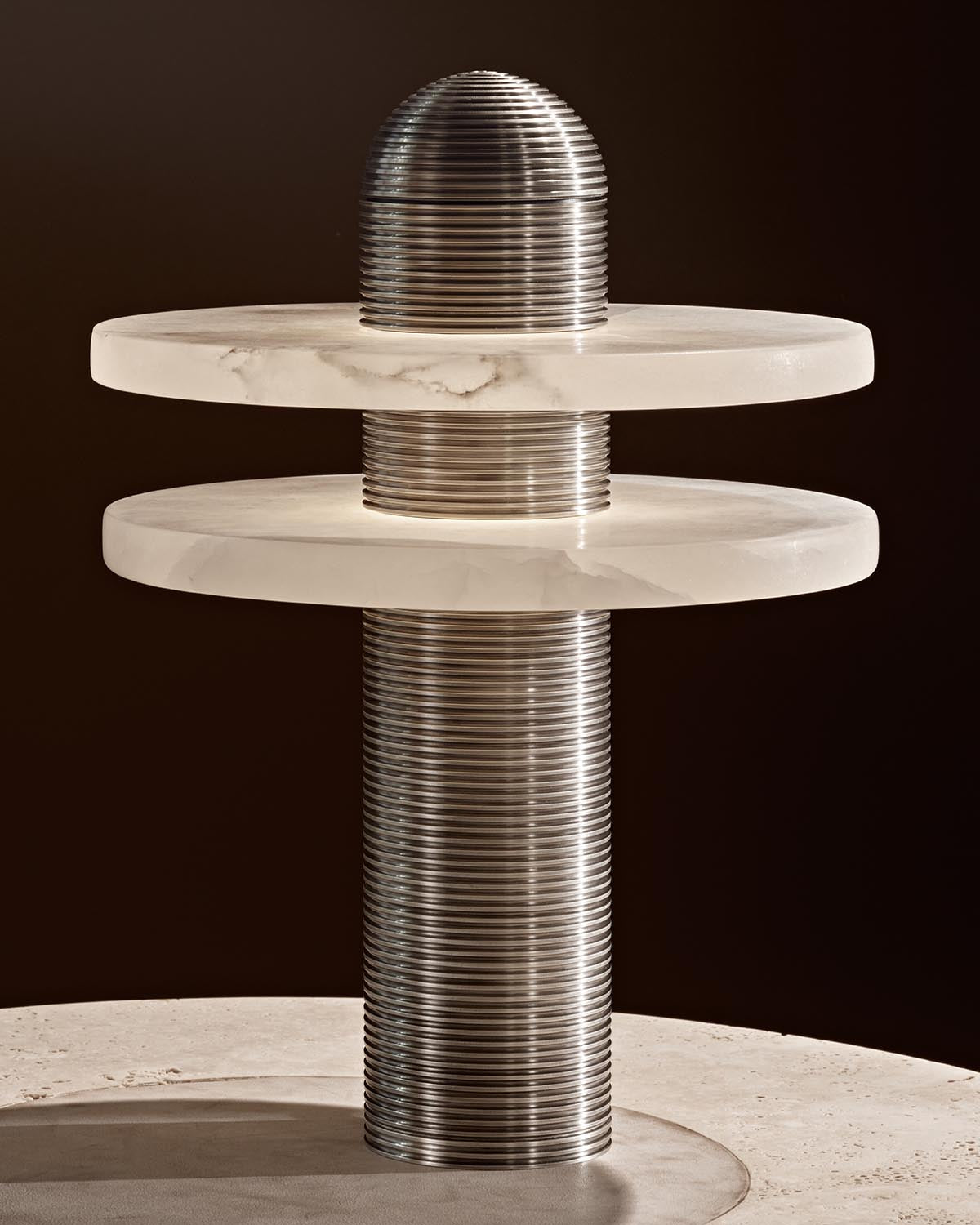 Close-up of modern table lamp with ribbed metallic cylindrical base and two round cream marble discs against dark background
