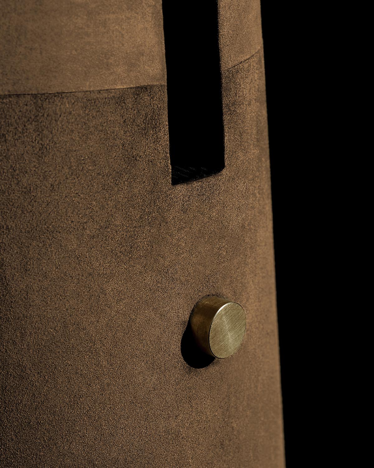 Close-up of brown suede floor lamp with cylindrical brass knob and black vertical slit on a black background