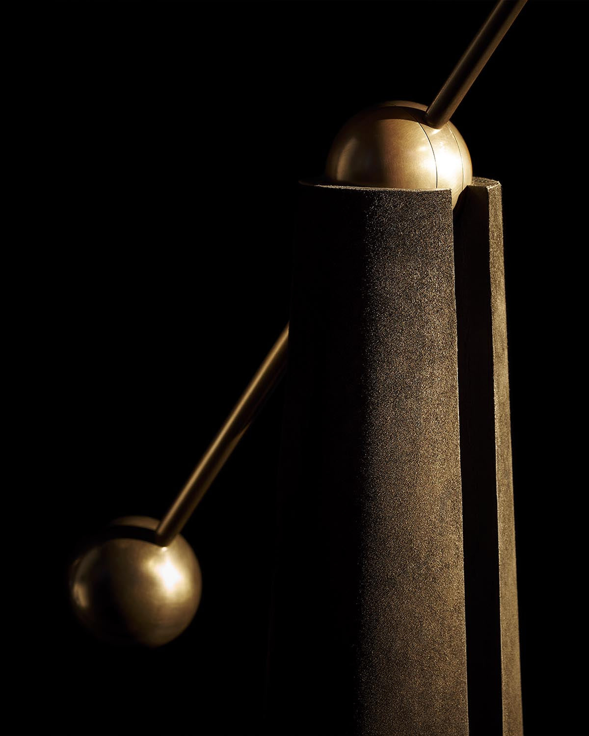 Close-up of a textured dark rectangular base with two metallic spheres connected by a slender rod on a black background
