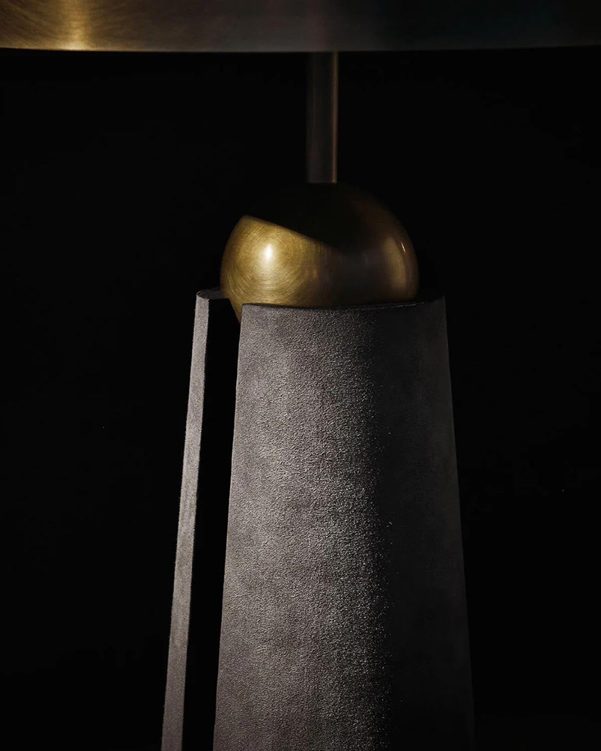 Close-up of a textured dark gray cylindrical lamp base with a smooth brass spherical element against a black background