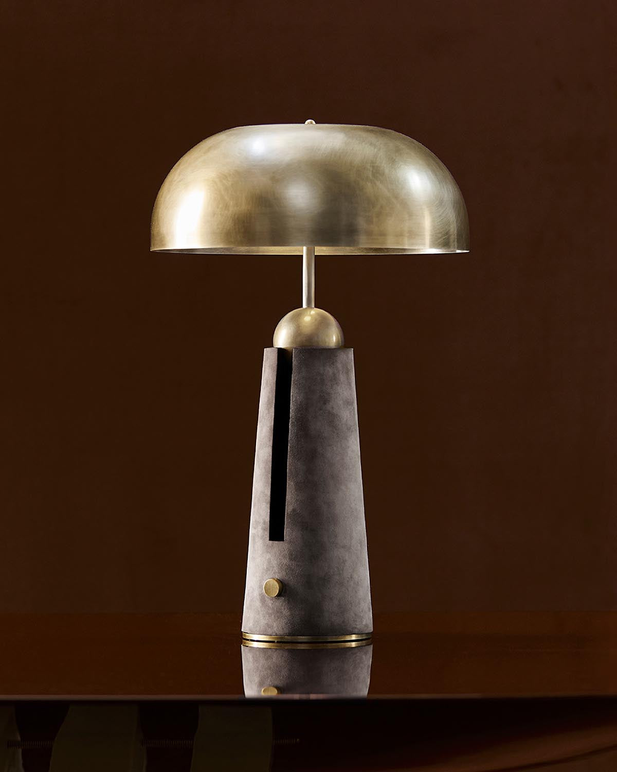 Table lamp with a matte brass dome shade and tapered concrete base featuring a vertical black slot and brass accents