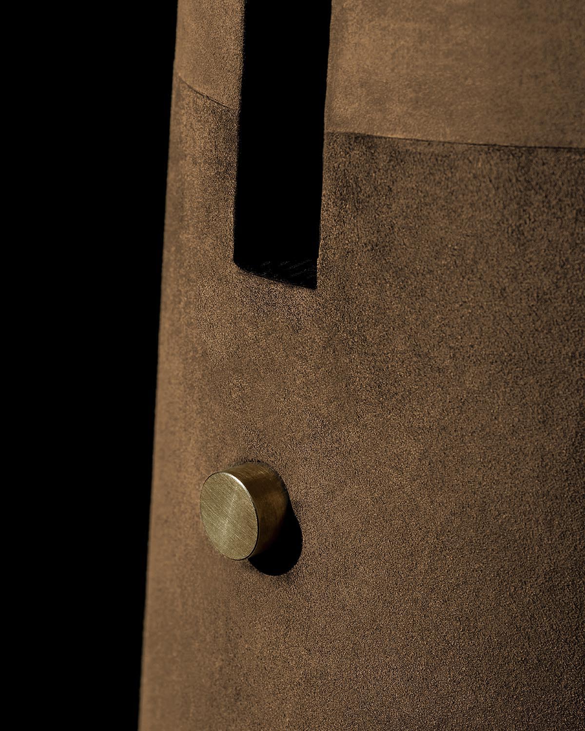 Close-up of brown textured lamp body with a round brass knob and vertical rectangular cutout on a black background