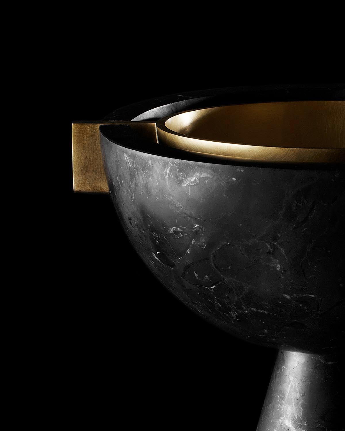 Close-up of a matte black vessel with smooth golden interior and a geometric handle against a black background