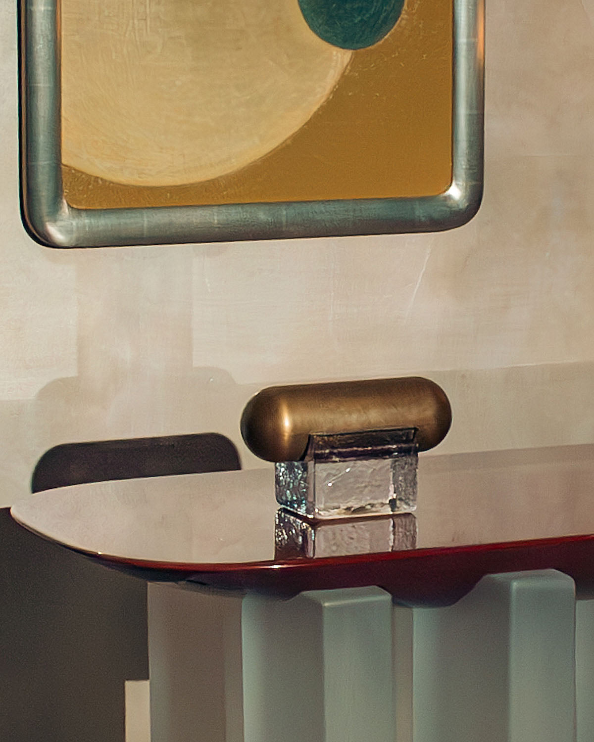 Close-up of a glossy rounded-edge table with a glass and bronze decorative object and abstract artwork in the background