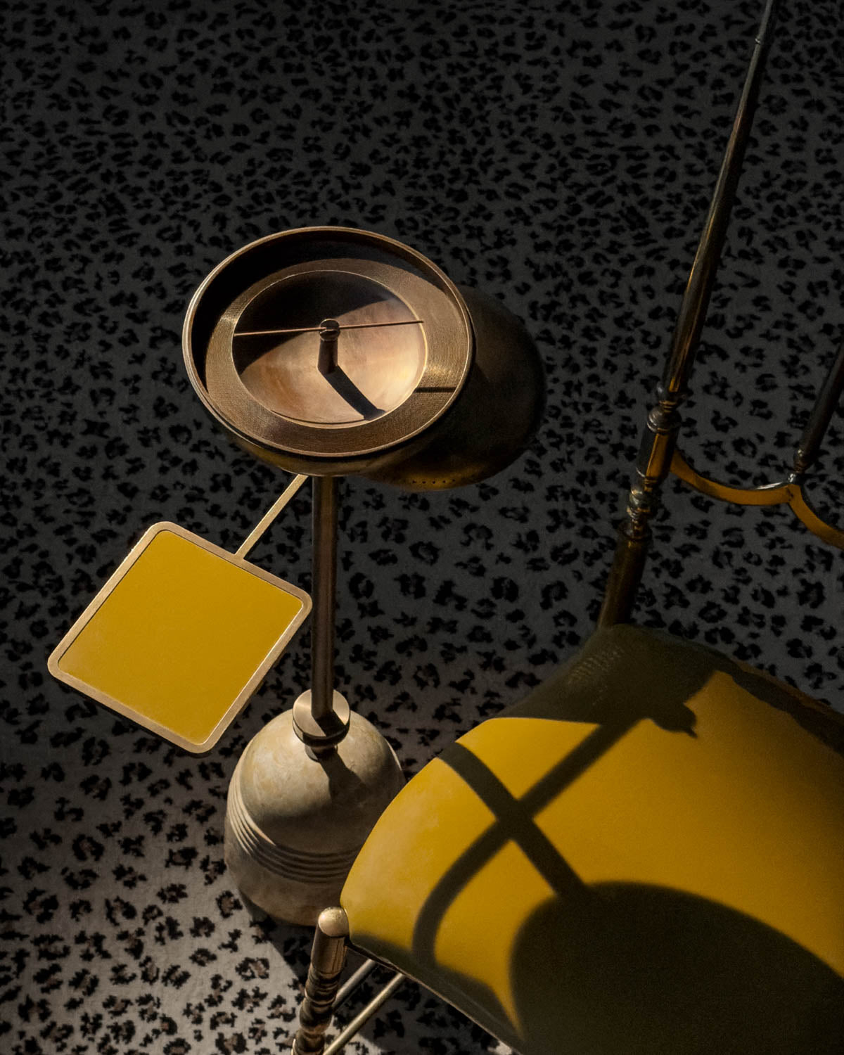 Top-down view of a vintage brass smoking table with attached ashtray and yellow side tray on patterned carpet