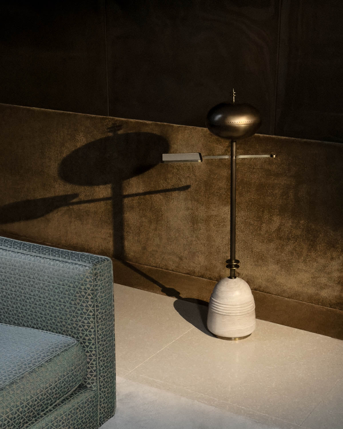 Modern smoking table with rounded dark metallic top and arms, supported by a ribbed light stone base against a textured wall