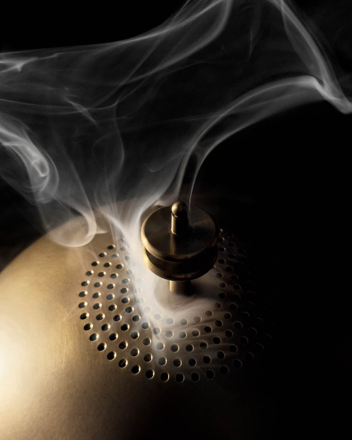 Close-up of brass smoking table surface with perforated details and curling smoke against a dark background