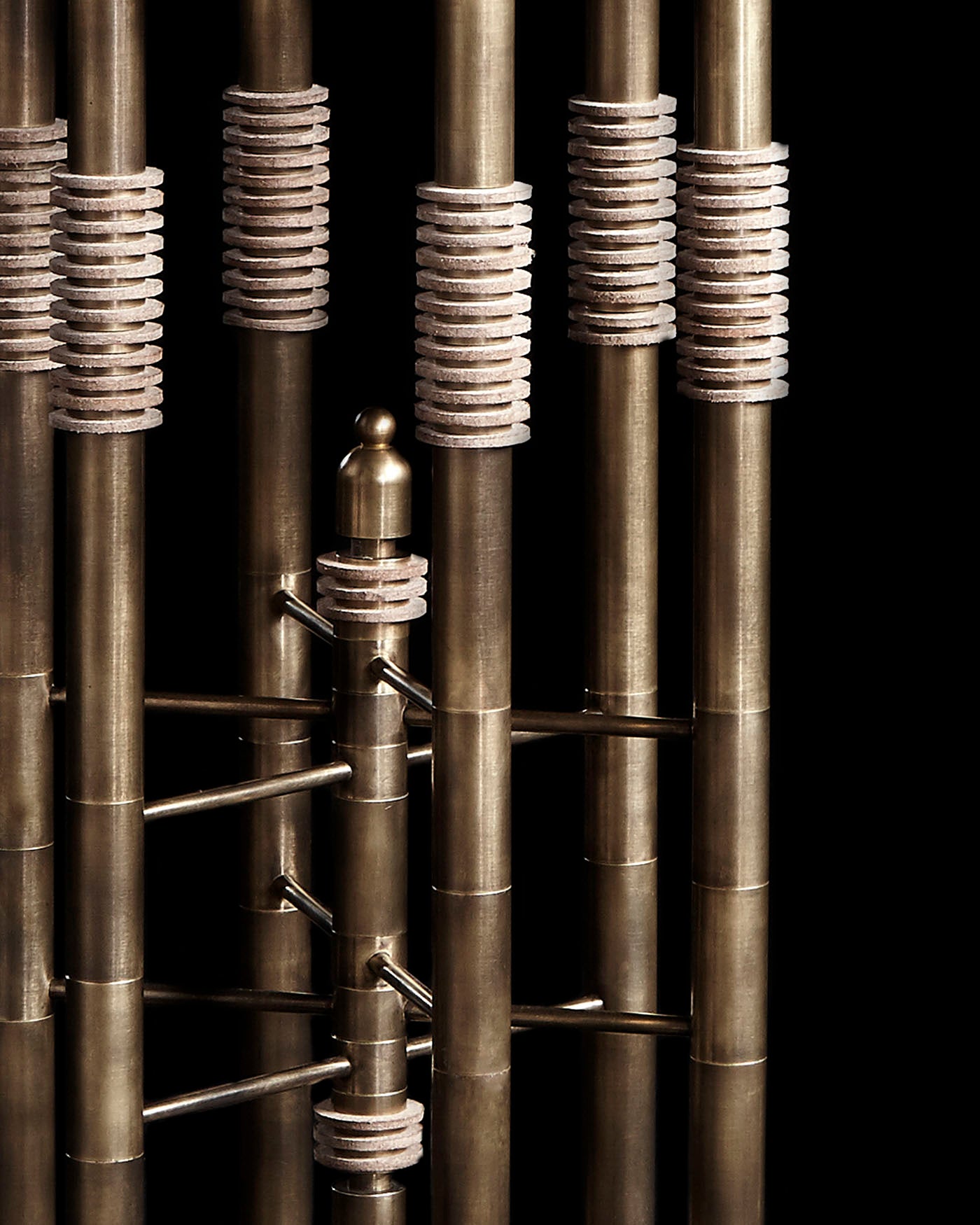 Close-up of metallic cylindrical table legs with textured leather rings and horizontal connectors in an industrial design against black background